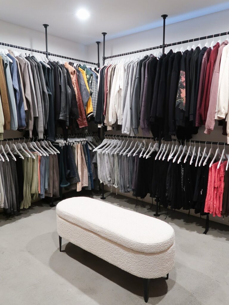 Two levels of black hanging rods filled with various clothes and white hangers in a closet.