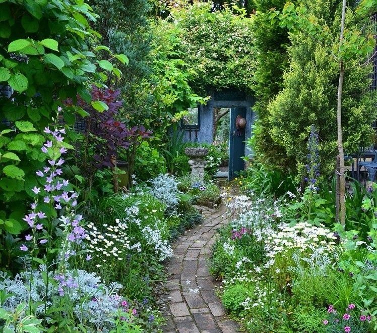 A winding brick pathway through a lush cottage garden filled with colorful flowers and green plants.