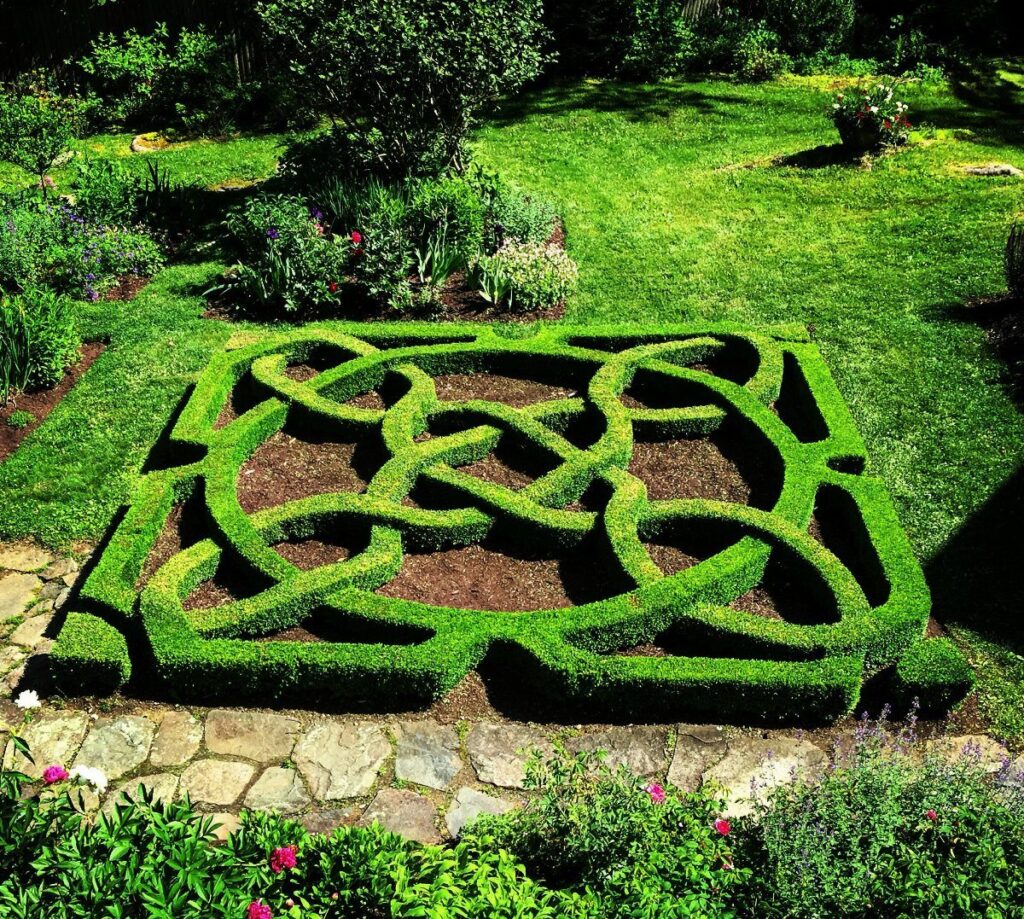 A formal knot garden featuring intricate green hedge patterns set in a lush outdoor landscape.