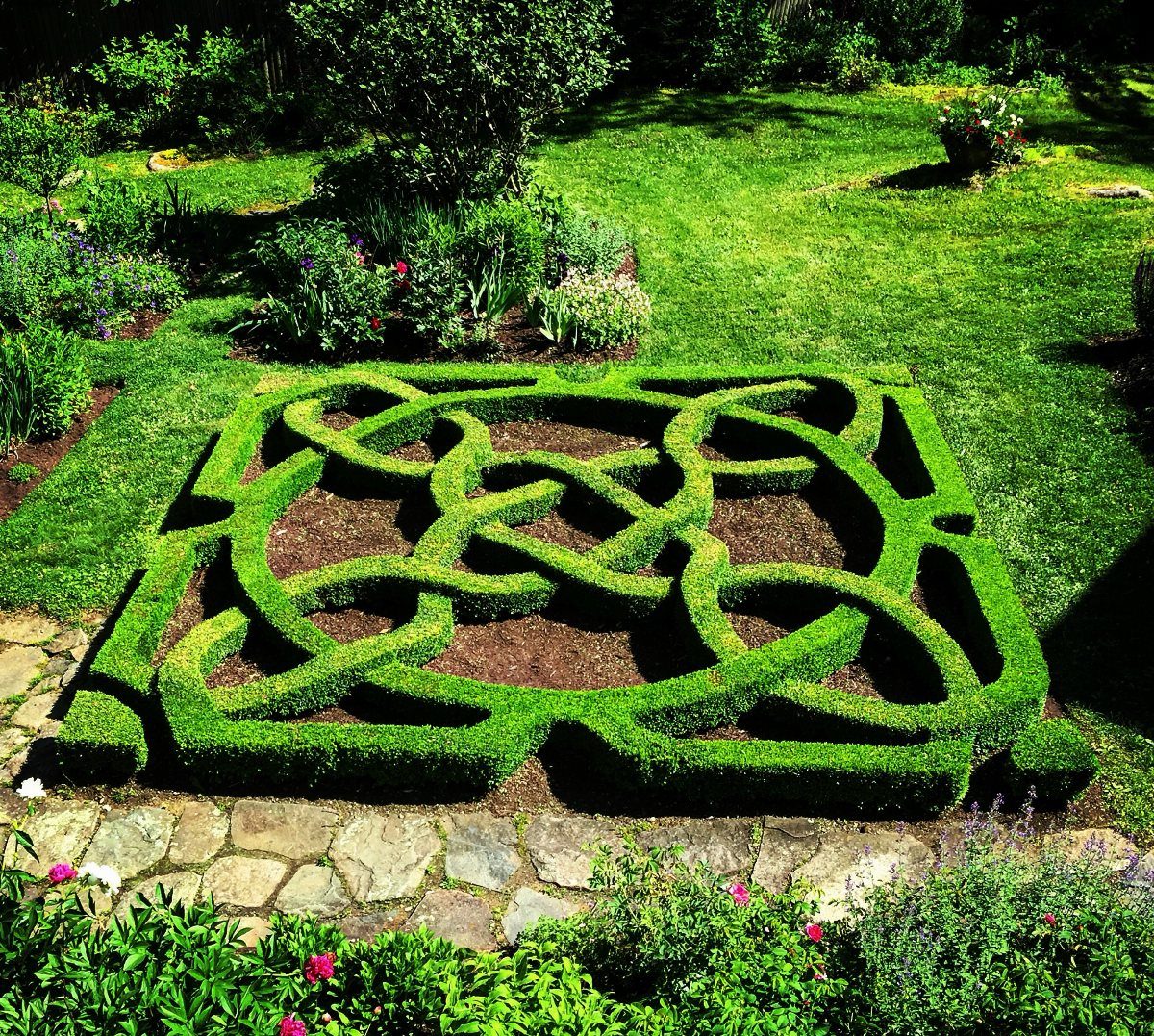 A formal knot garden featuring intricate green hedge patterns set in a lush outdoor landscape.