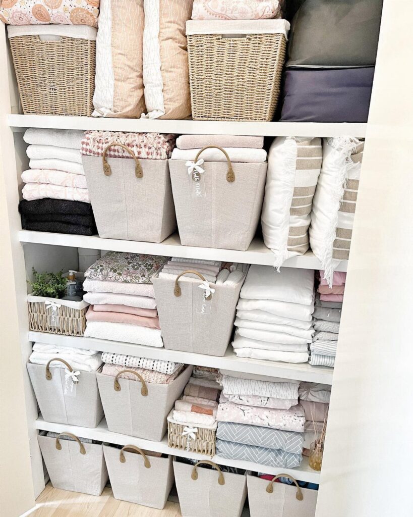 White shelves holding numerous fabric and wicker baskets filled with neatly folded linens and pillows.