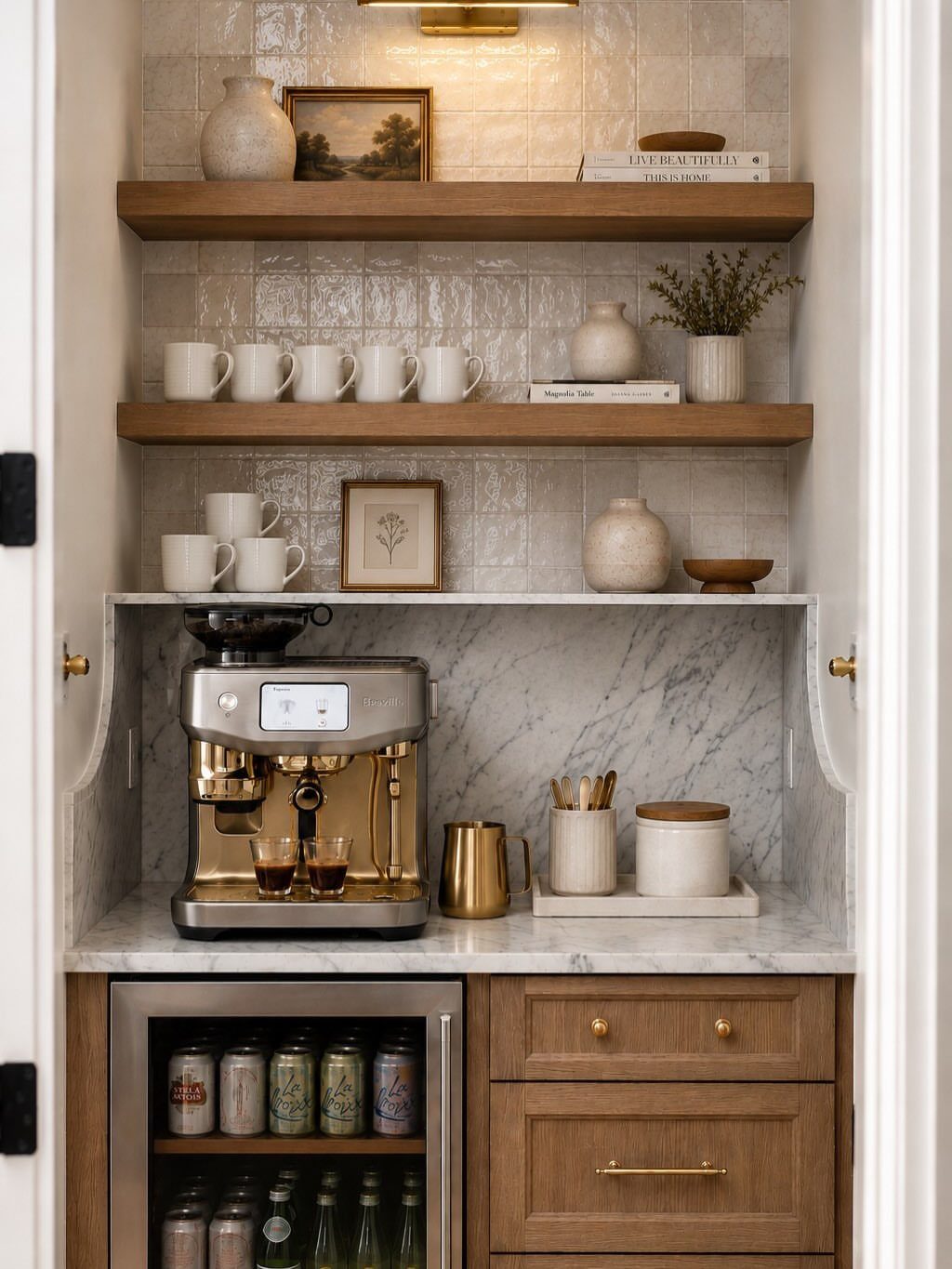 A marble countertop coffee station with an espresso machine, wooden shelves, and mugs against tiled walls.