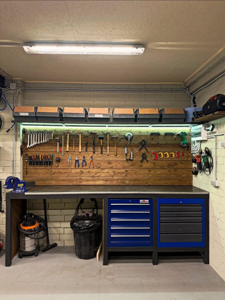 A wooden workbench with a grey top, blue tool chests, and various hand tools hanging on a wall.