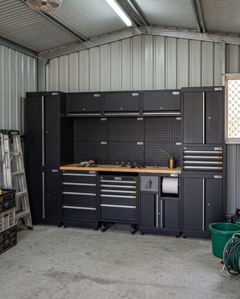 Black metal garage storage cabinets and workshop workbench with tools against a corrugated wall.