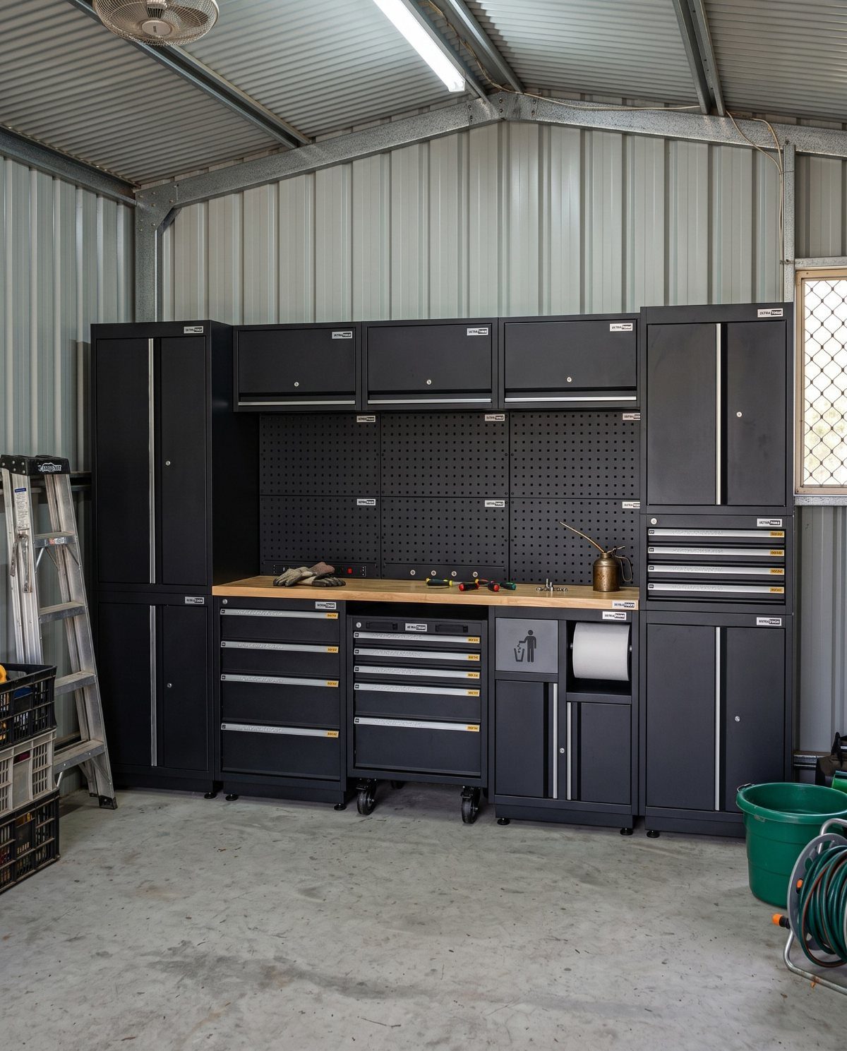 Black metal garage storage cabinets and workshop workbench with tools against a corrugated wall.