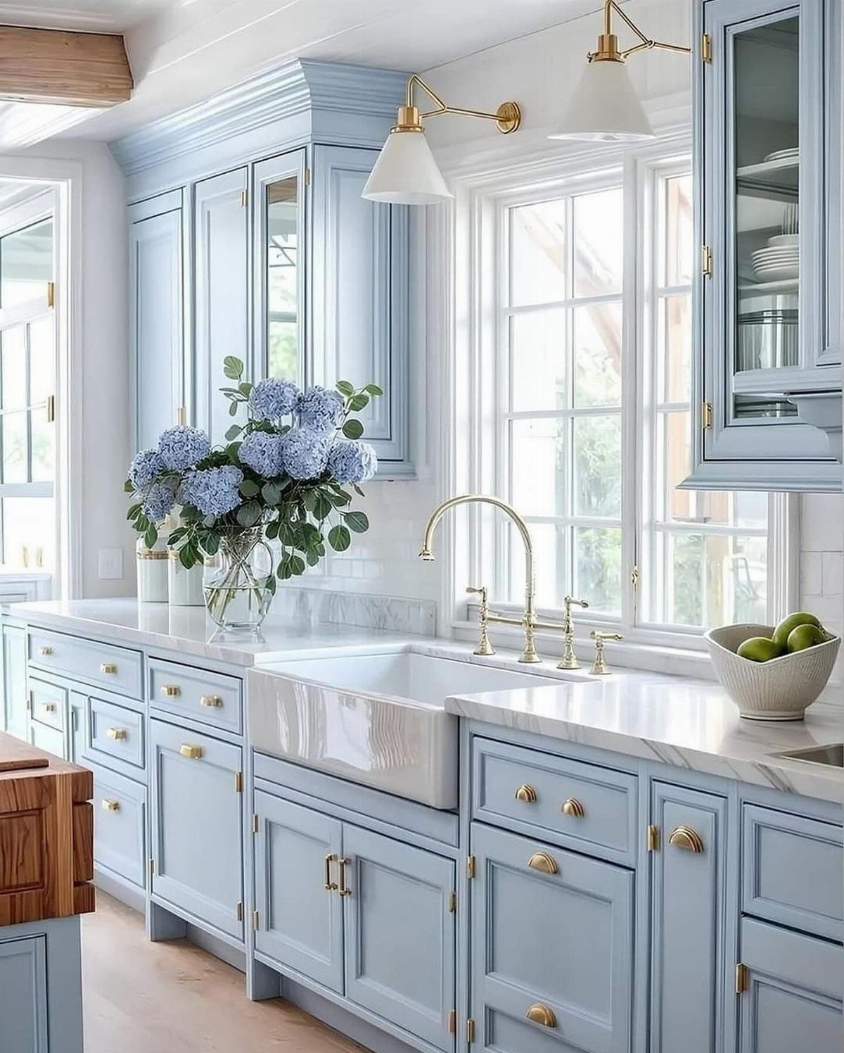 Light blue kitchen cabinets with marble countertops and gold hardware featuring blue hydrangeas.