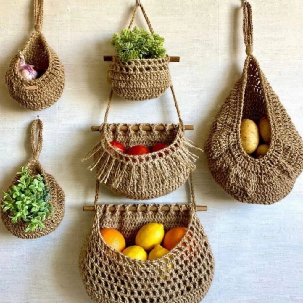 Woven jute hanging baskets containing garlic, plants, tomatoes, and citrus fruits mounted on a wall.