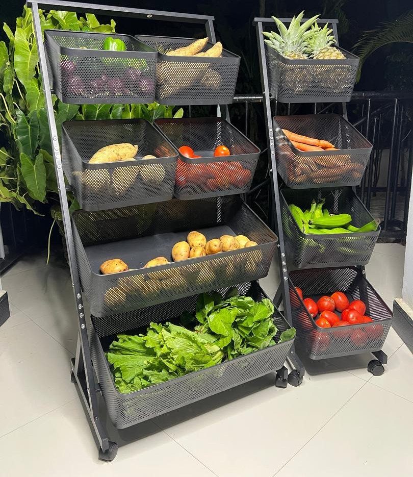 Two black metal tiered storage racks filled with various fresh vegetables on a tiled floor.