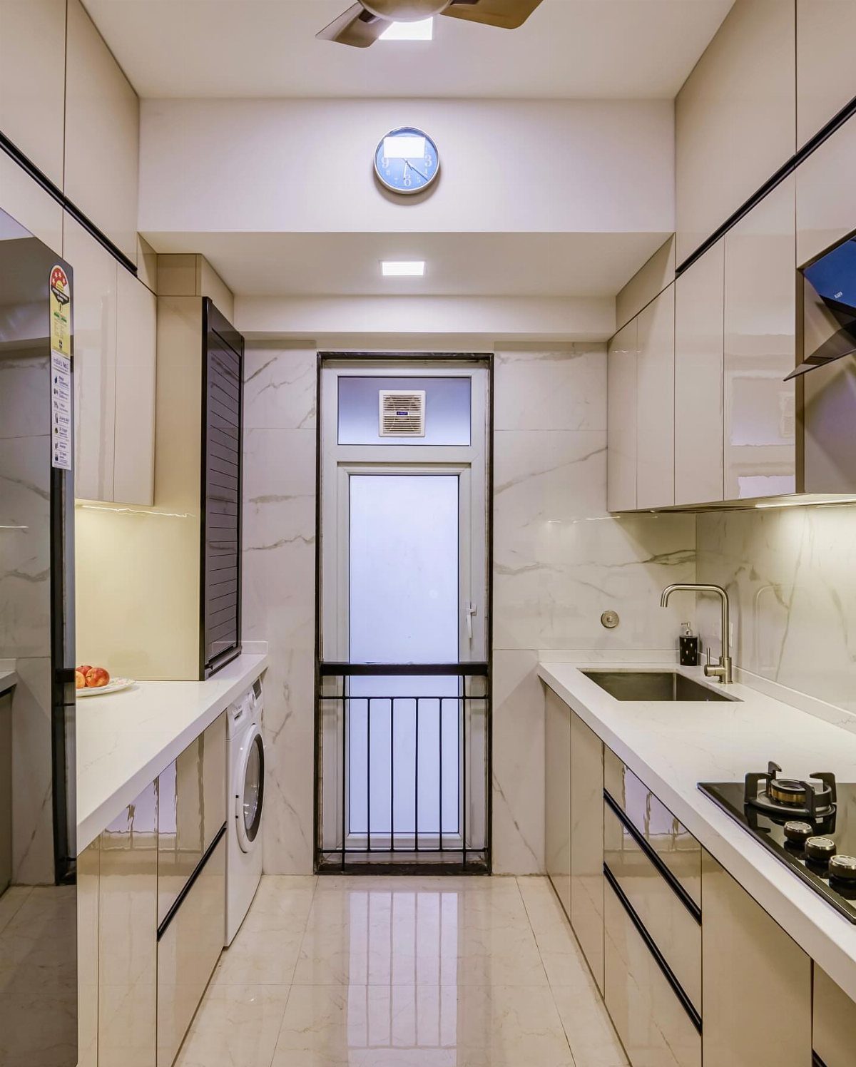 A narrow parallel kitchen with white countertops, cream cabinets, and marble-patterned walls.
