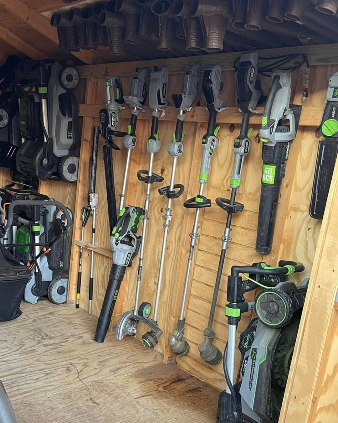 Cordless yard tools hanging organized on a wooden wall in a storage shed.