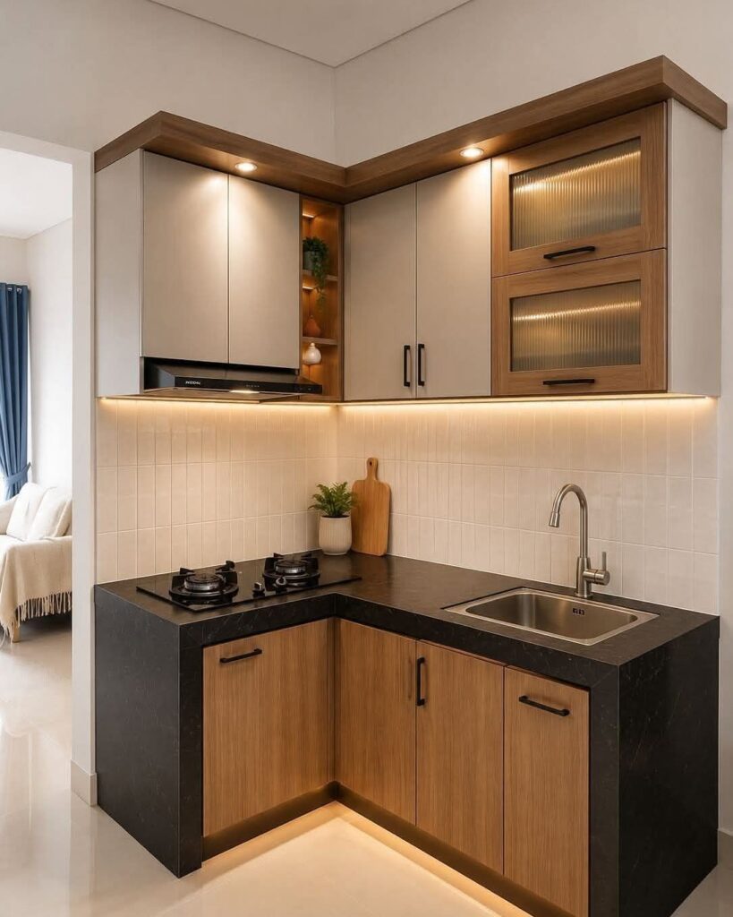 Small L-shaped kitchen with grey and wood cabinets, black countertops, and warm under-cabinet lighting.