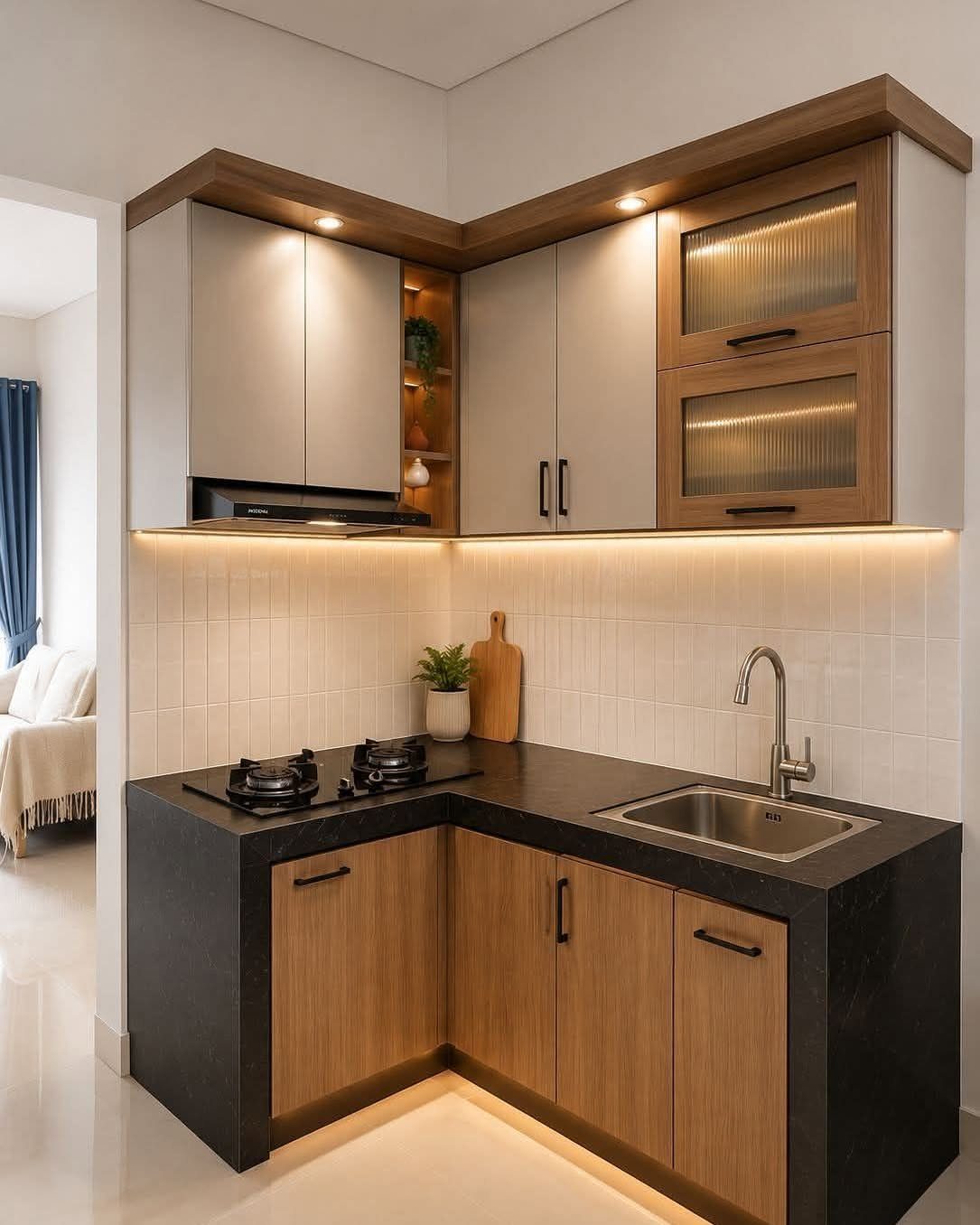 Small L-shaped kitchen with grey and wood cabinets, black countertops, and warm under-cabinet lighting.
