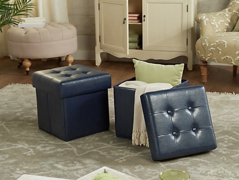 Two navy blue tufted leather storage ottomans on a patterned rug in a living room.