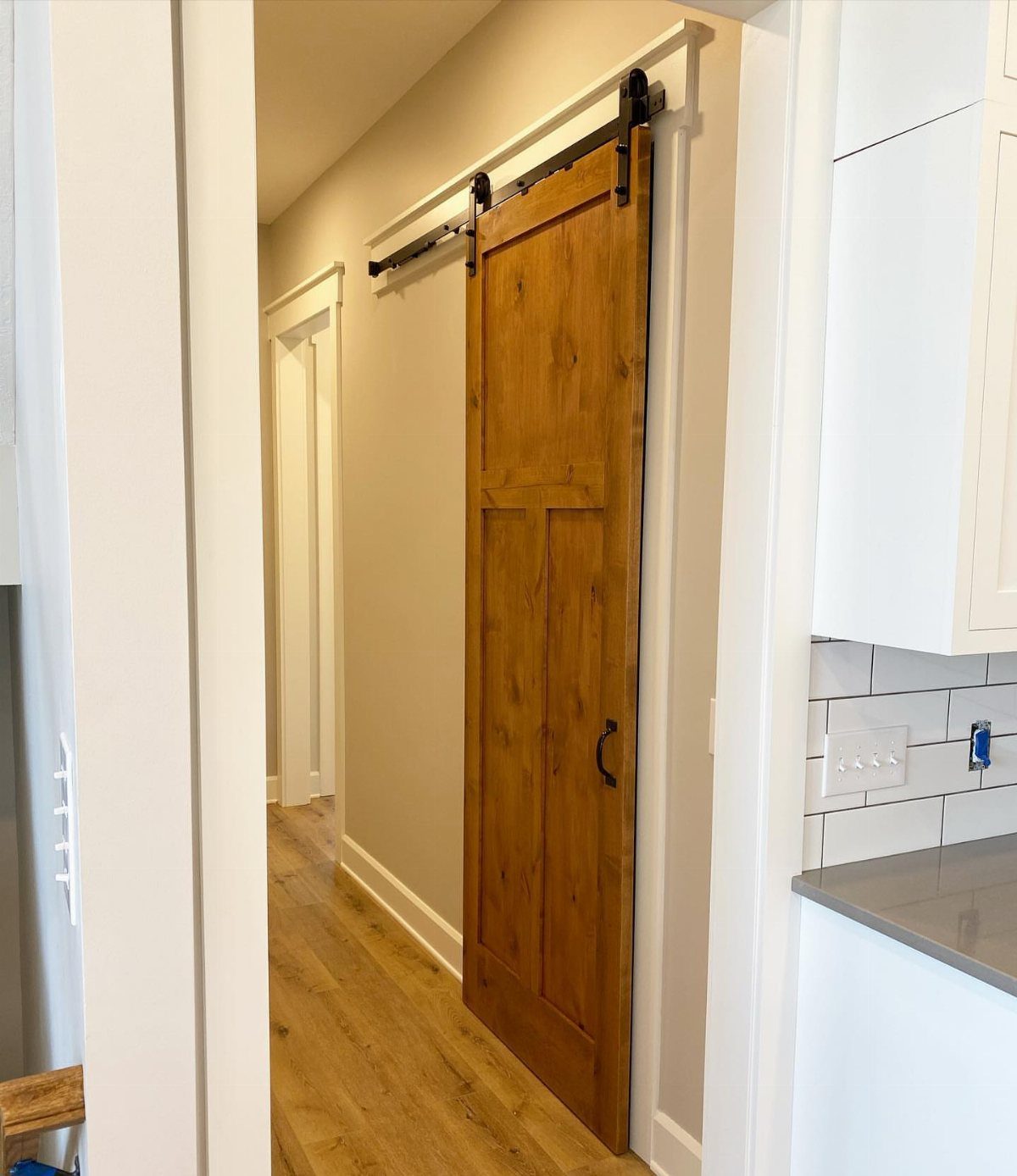 A wooden sliding barn door with black metal hardware mounted on a white wall.