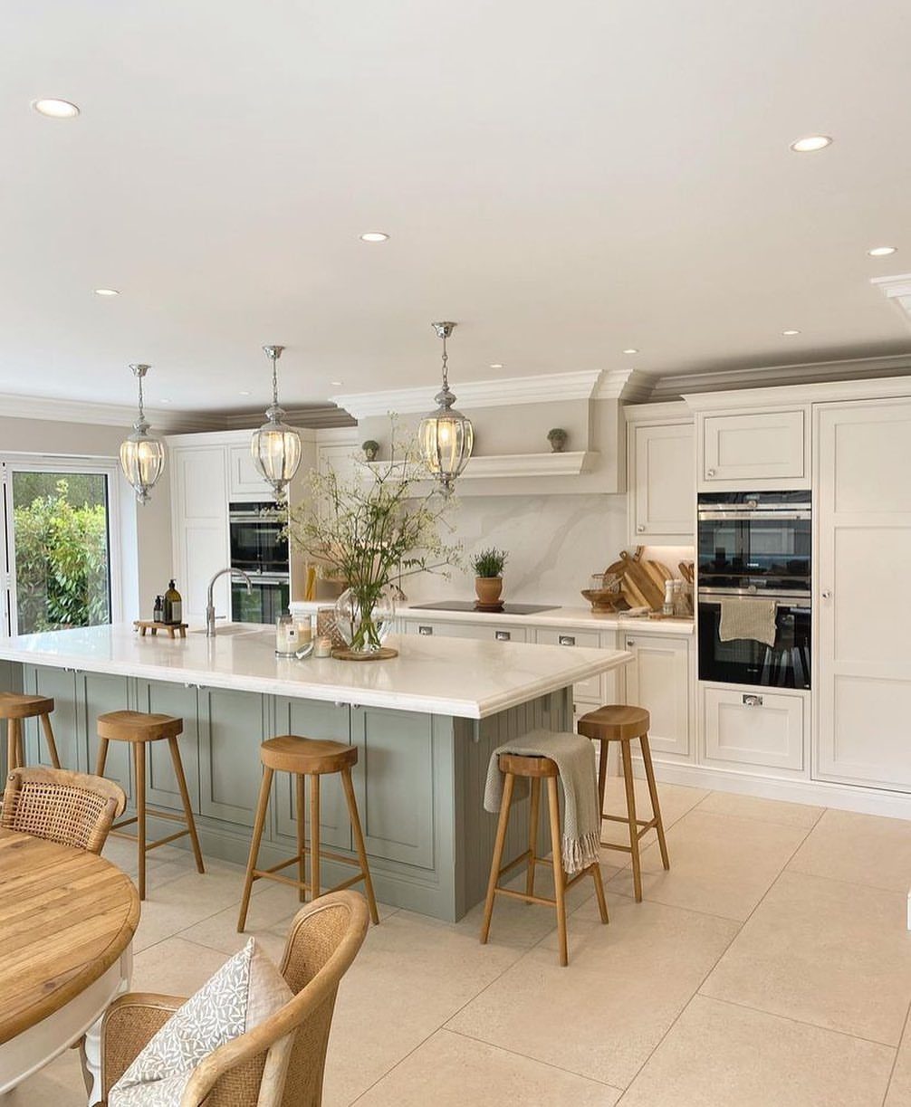 A sage green kitchen island with a white marble countertop and wooden stools in a bright kitchen.