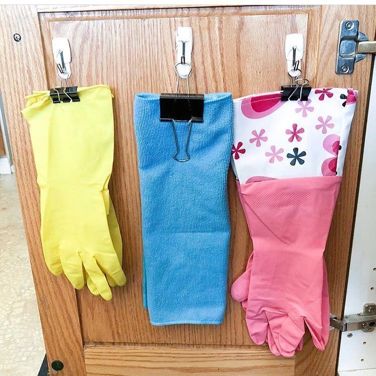 Yellow, blue, and pink rubber gloves hanging from white hooks on a wooden door.